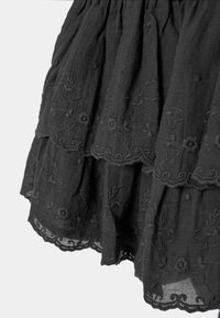 Tissu noir avec broderie florale en couches et bords festonnés, montrant une texture délicate et des détails complexes.