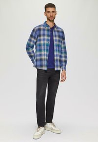 Ruudullinen pitkähihais shirt sinisen, vihreän ja valkoisen sävyissä, kerrostettuna tummansinisen t-paidan päälle. Mustat farkut ja valkoiset lenkkarit viimeistelevät asun.