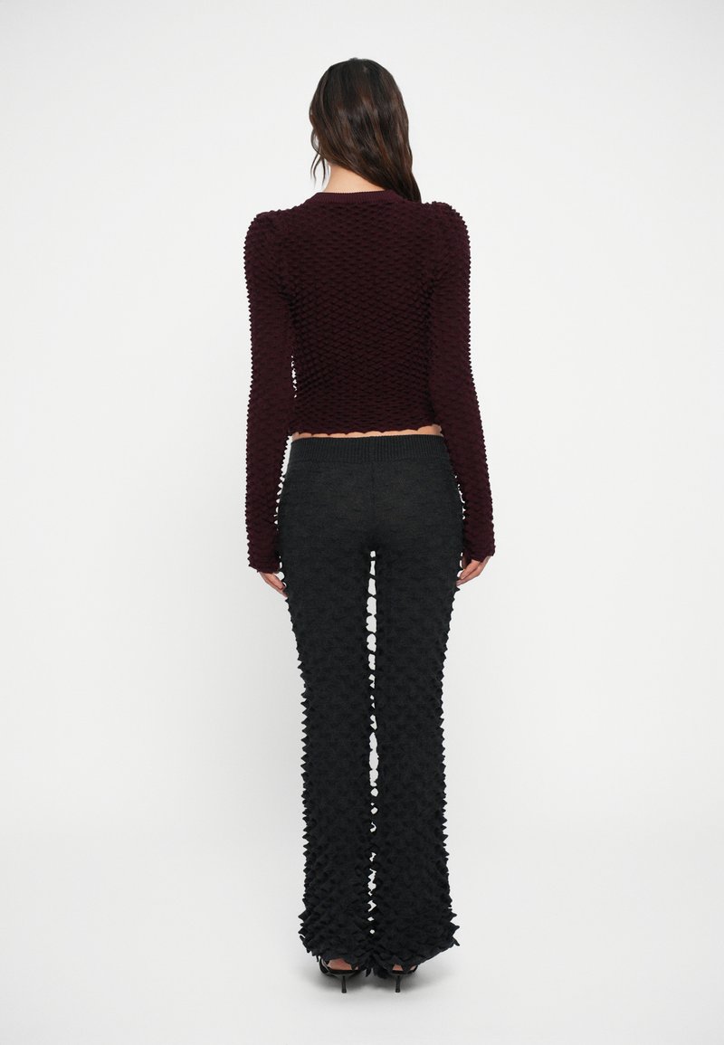 Top a maniche lunghe marrone ramato con texture, abbinato a pantaloni neri a campana con una texture simile. L'outfit ha uno stile aderente con una lunghezza cropped.