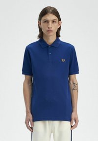 Polo di colore blu navy con colletto classico, maniche corte e logo ricamato in oro sul lato sinistro del petto. Tessuto morbido al tatto, taglio dritto.