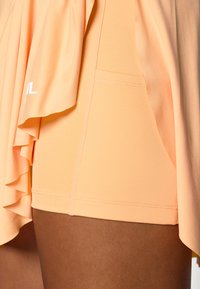 Persikofärgade sportshorts med en rufsig överdel, gjorda av ett mjukt tyg. Har en sidficka och sömnadsdetaljer.