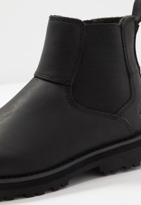 Bota de tornozelo em couro preto com painéis laterais elásticos, sola de borracha robusta e detalhes de costura distintos ao longo das costuras.