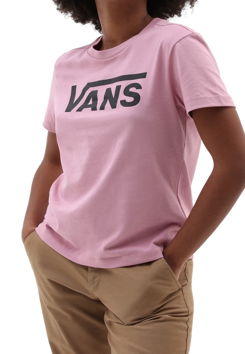 Světle růžové tričko s krátkým rukávem a černým logem Vans na přední straně. Má klasický kulatý výstřih a volný střih.