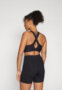 Sort sports-bh med kryssrygg-design og nøkkelhull-detall, kombinert med høytopp svarte shortser. Myk, elastisk stoff, minimalistisk utseende.