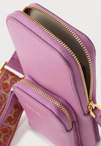 Mala tiracolo roxa em couro com dois compartimentos com fecho de correr e acabamento texturizado. Apresenta ferragens douradas e uma alça de tecido padronizada.