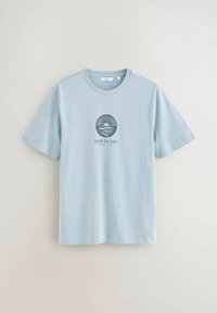 Lichtblauw T-shirt met korte mouwen en een ronde halslijn, voorzien van een cirkelvormige zonsondergang- en oceaangrafiek en de tekst "Chasing Blue Echoes" op de borst.