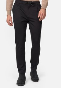 Pantalones negros de corte slim, con cintura ajustable mediante cordón y bolsillos laterales, hechos de una tela suave y elástica. Combinados con botas negras hasta el tobillo.