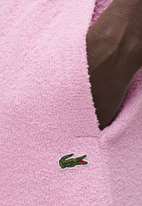 Vêtement en éponge rose avec une finition texturée. Comprend un logo crocodile brodé en vert et rouge sur le devant.