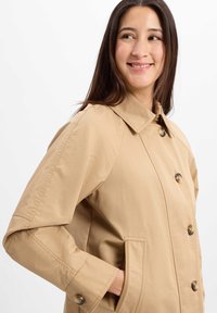 Hellbeige, knöpfbarer Mantel mit umgeschlagenem Kragen, seitlichen Taschen und glatter Textur. Verfügt über Raglanärmel und dekorative Knöpfe.