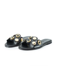 Schwarze Ledersandalen mit einem breiten Riemen, der mit kreisförmigen, metallischen Akzenten in Gold und Blau geschmückt ist. Flache Sohle mit sichtbaren Nahtdetails.