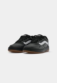 Black sneakers with a smooth leather upper, white wave accent, and brown rubber sole. Features lace-up closure and padded collar.