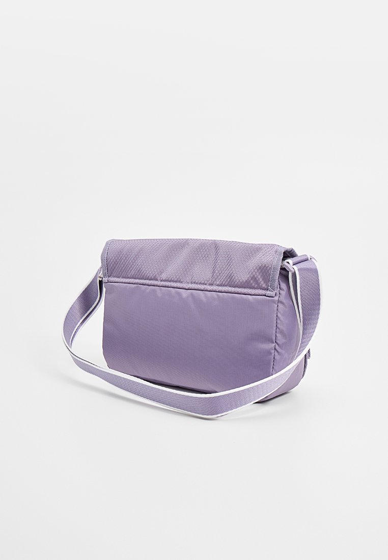 Bolso de hombro lila con correa ajustable, cierre de solapa y textura de tela suave, mostrado sobre un fondo blanco liso.