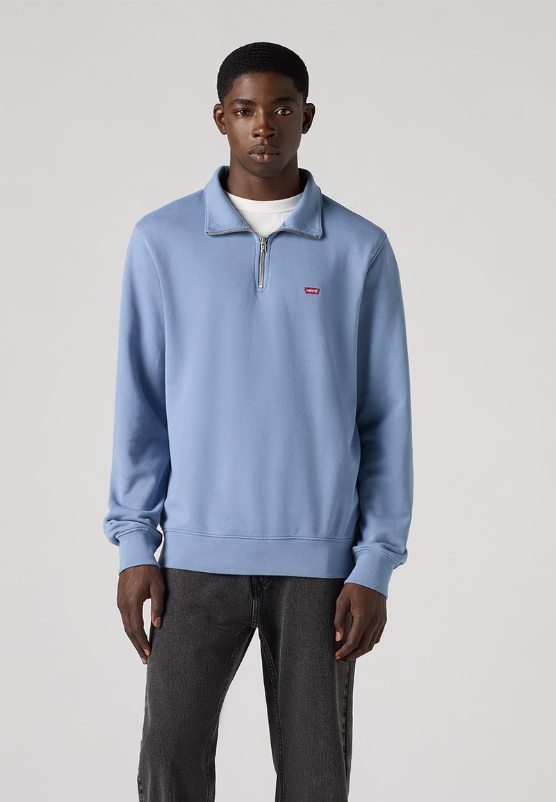 Hellblaues Sweatshirt mit halbem Reißverschlusskragen, gerippten Bündchen und Saum. Kleines rotes Logo auf der linken Brust. Weicher Stoff.