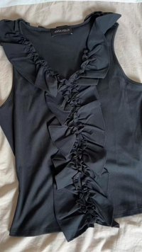 Černý top bez rukávů s vroubkovanou texturou, který má centrální volánový design od výstřihu až k lemu a široké volánové ramenní popruhy.