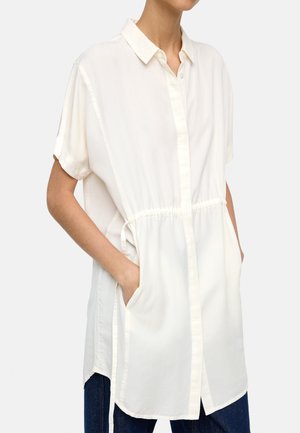 Biała koszula z krótkim rękawem, zapinana na guziki, z paskiem ściągającym w talii i bocznymi kieszeniami. Wykonana z lekkiego, gładkiego materiału.