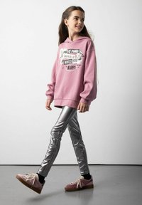 Różowa bluza z kapturem z graficznym napisem, srebrne legginsy i różowe sneakersy. Bluza ma luźny krój i mankiety. Gładka metaliczna faktura legginsów.