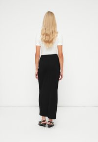 Zwarte maxi rok met een aansluitende taille, een gladde textuur en een lichte split, gecombineerd met een witte aansluitende top en zwarte hoge hakken.