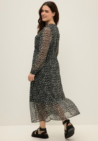 Vestido midi negro con estampado floral blanco, mangas largas transparentes, cintura ajustada y dobladillo con volantes. Combinado con sandalias negras con tiras.