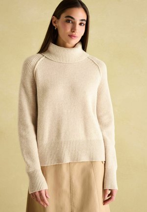 Maglione a collo alto crema con texture a coste, vestibilità rilassata e maniche lunghe. Il materiale in maglia morbida conferisce un aspetto accogliente.