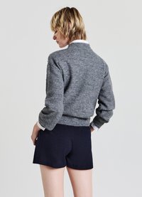 Grauer Strickpullover mit hohem Kragen und geripptem Saum, kombiniert mit marineblauen Shorts mit einem strukturierten Muster. Sichtbare weiße Hemdsärmel.