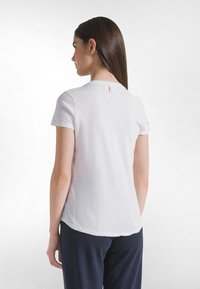 Camiseta blanca de manga corta con cuello redondo, con un acabado texturizado y una pequeña etiqueta de tela en la parte trasera del cuello.