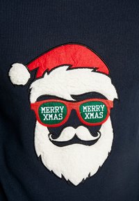 Jersey navy con una cara festiva de Santa que lleva un gorro rojo, barba blanca de peluche y gafas de sol verdes con el texto "FELIZ NAVIDAD".