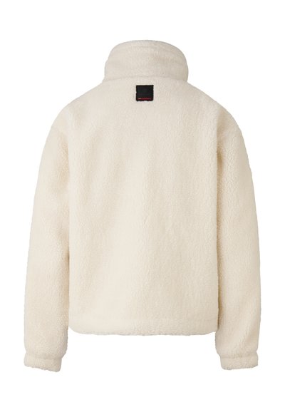 Fløjljakke i cremefarve, blød tekstur, høj krave og et firkantet sort mærke med røde accenter bagpå. Casual design uden synlige lukninger.