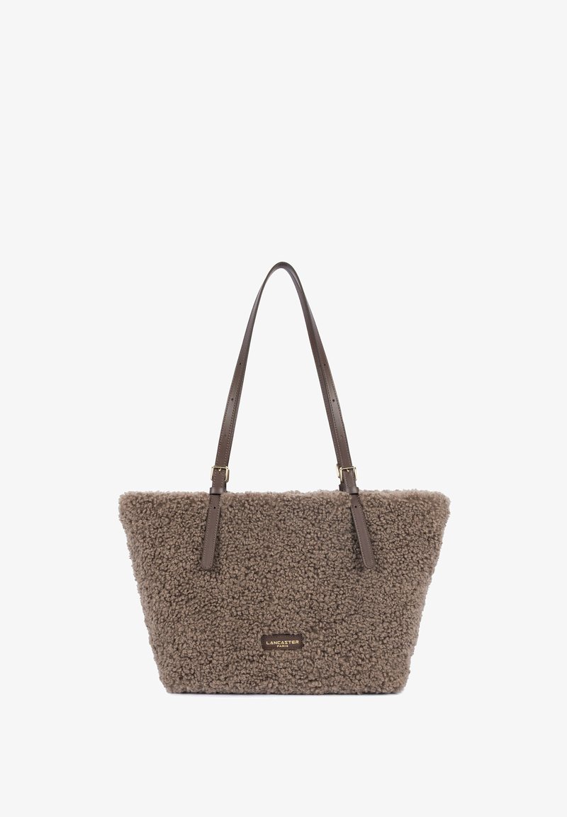 Sac cabas marron texturé avec de longues bretelles en cuir marron foncé et une petite étiquette rectangulaire de marque à l’avant.
