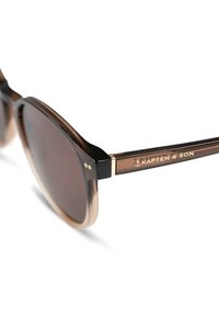 Braune Verlaufssonnenbrille mit einem Schildpatt-Rahmen, verziert mit goldenen Akzenten und einem Logo am Bügel. Die Gläser sind dunkel und rund.