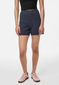 Shorts en tricot marine avec taille côtelée, ourlet à volants et un motif texturé, associés à des baskets roses.