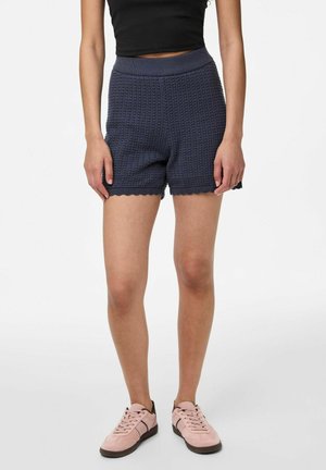 Marineblå strikkede shorts med ribbet talje, bølget kant og et struktureret mønster, parret med lyserøde sneakers.