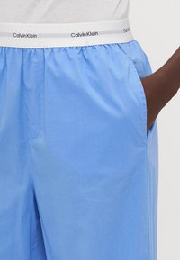 Lichtblauwe shorts van gladde stof, met een witte elastische tailleband met het "Calvin Klein" logo en zijzakken.