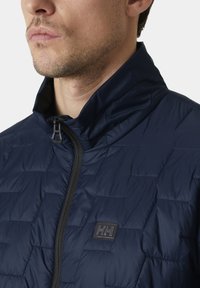 Navy puffer bunda s vysokým límcem, prošívanou strukturou a černým zipem. Obsahuje nášivku s logem na hrudi a hladkou, voděodolnou tkaninu.