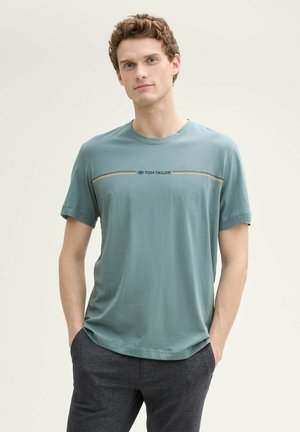 Camiseta de algodón en color verde azulado con cuello redondo, mangas cortas y un diseño de rayas horizontales encima del pecho que presenta "TOM TAILOR" en texto negro.