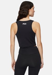 Top corto negro de tirantes con textura suave y escote redondeado. Presenta un logotipo blanco de FILA en la parte posterior y se combina con unas leggings negras de cintura alta.