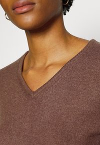 Brun v-ringad tröja i mjukt, strukturerat tyg. Nära bild framhäver halslinjen och subtila sömnadsdetaljer.