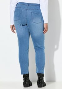 Vaaleansinisen denimin kapeat farkut, joissa on kaksi takataskua ja sileä pinta, yhdistetty mustiin niitattuihin nilkkureihin.