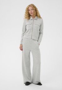 Sivý zipsový sveter s dvoma náprsními vreckami v kombinácii s nohavicami s širokými nohavicami. Mäkko látku a uvoľnený strih po celom oblečení.