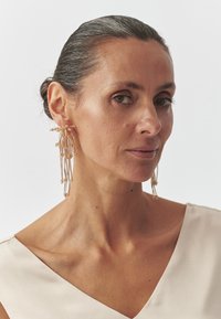 Koronne korvakorut, joissa on useita pitkänomaisia metallilangat, koristeltuna pienillä helmillä lisäämään tekstuuria ja yksityiskohtia.