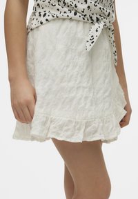 Gonna mini bianca e testurizzata con orlo arricciato. Realizzata in un tessuto leggero, presenta un design stropicciato e una vita elastica.