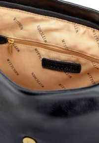 Interior de bolsa de cuero negro con bolsillo con cremallera dorada y forro marrón claro que presenta un patrón repetido de "WITTCHEN". Textura suave y diseño elegante.
