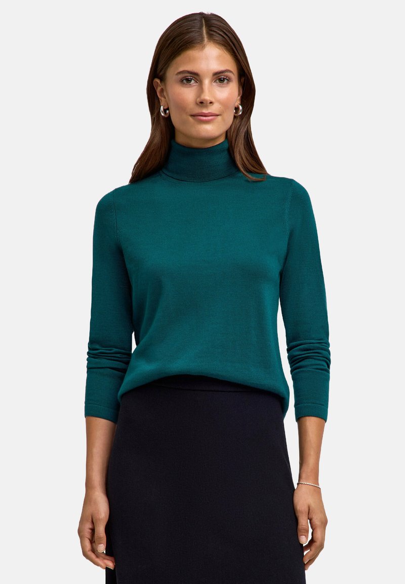 Türkiser Rollkragenpullover mit langen Ärmeln, weicher Textur und taillierter Passform. Kombiniert mit einem schwarzen Rock. Schlichte und klare Linien.