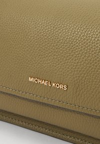 Olivengrønn skinnhåndveske med teksturert overflate og gullfarget "MICHAEL KORS"-logo. Har ren søm og en strukturert design.