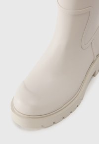 Beżowe, wodoodporne buty z gładkim, błyszczącym wykończeniem, okrągłym noskiem i grubą gumową podeszwą z głębokimi bieżnikami dla lepszej przyczepności.
