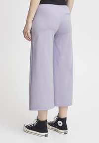 Lila wijde broek gemaakt van zachte stof met een gladde textuur, met een achterzak en een relaxte pasvorm. Gepaard met zwarte hoge sneakers.