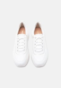 Ζευγάρι λευκά δερμάτινα αθλητικά παπούτσια με κορδόνια, μπεζ εσωτερικά πέλματα και στρογγυλεμένη μύτη, εμφανιζόμενα από επάνω σε απλό φόντο.