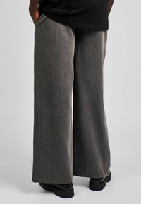 Pantaloni largi dintr-un material texturat gri. Prezintă un talie înaltă, buzunare laterale și o croială lejeră, asortați cu bocanci negri masivi.