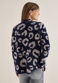 Námořnický modrý svetr se šedým leopardím vzorem, měkká textura, kulatý výstřih a volný střih. Žebrované manžety a detail lemu.