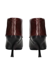 Zwarte leren hakken met een glanzende bordeauxrode enkelband, met een spitse neus en slanke stilettohak. Glad oppervlak, minimalistisch ontwerp.