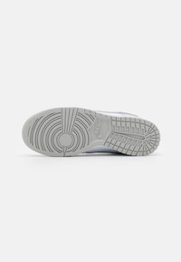 Semelle d'une basket Nike gris clair avec des motifs de bande de roulement circulaires et rectangulaires ainsi que le logo Nike embossé au centre.
